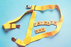 Happy Father's Day Schriftzug aus Holzwürfeln auf blauem Hintergrund mit gelben Hosenträgern foto