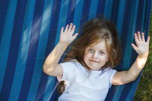 Porträt eines kleinen süßen Mädchens mit langen Haaren, das auf einer Hängematte im Garten ruht und lächelt foto