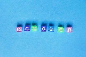 inschrift oktober aus mehrfarbigen plastikwürfeln auf blauem hintergrund. foto