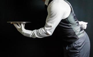 Porträt eines eleganten Butlers oder Kellners in Weste und weißen Handschuhen mit silbernem Serviertablett. bei Ihrem Servicekonzept. professionelle Gastfreundschaft. foto