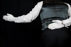 butler oder kellner in weißen handschuhen, die sich mit einladender geste auf schwarzem hintergrund verbeugen. Konzept der Dienstleistungsbranche und professionelle Gastfreundschaft und Höflichkeit. foto
