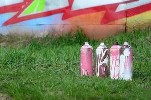 Ein paar gebrauchte Farbdosen liegen auf dem Boden in der Nähe der Wand mit einem schönen Graffiti-Gemälde. Straßenkunst- und Vandalismuskonzept foto