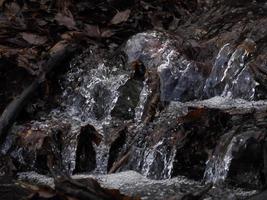 kleiner fließender Fluss aufgrund der Schneeschmelze, der eine saubere Kaskade mit frischem, kühlem Wasser bildet, umgeben von einem Vegetationsberg foto
