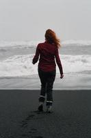 frau, die am strand von reynisfjara szenische fotografie entlang geht foto