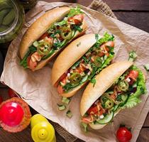 Hot Dog mit Jalapenopfeffer, Tomaten, Gurken und Salat auf Holzhintergrund foto