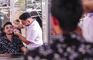 gutaussehender arabischer mann wird vom friseur im friseursalon rasiert foto