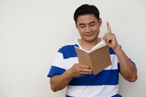 hübscher asiatischer mann liest buch und zeigt mit dem zeigefinger nach oben. konzept, buch lesen, wissen und idee bekommen. Prüfung vorbereiten. Bildung. Hobby und Zeitvertreib. Lesen zum Vergnügen. Kopieren Sie Platz zum Hinzufügen von Text. foto