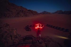 reisender träumer abenteurer in der wadi rum wüste bei nacht lichtmalerei wort jo als jordan mit herz. reise erkunden jordanien abenteuerkonzept foto