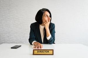 junge kaukasische brünette geschäftsfrau direktorin im büro schauen zur seite des leeren raums, der nachdenklich ist, treffen entscheidungen im büro allein am arbeitstisch foto