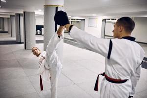 Junge Taekwondo-Kämpferin mit Behinderung, die mit ihrem Trainer im Fitnessclub High Kick übt. foto