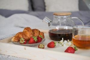 Frühstück im Bett. Tablett mit Tee, Croissant und Erdbeeren auf dem Bett im Schlafzimmer foto