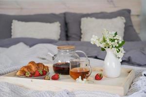 Frühstück im Bett. Tablett mit Tee, Croissant und Erdbeeren auf dem Bett im Schlafzimmer foto