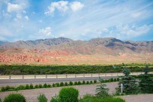 Bergschlucht mit roten Graten, Bäumen und Straße. Landschaft Kirgistans. Platz kopieren foto