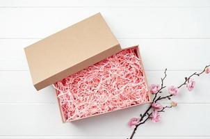 geschredderte rosa papierverpackungsmaterialstruktur in einer handwerksbox mit sakura-zweig, mockup-design foto