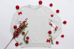 Schließen Sie herauf weißes leeres Schablonensweatshirt mit Kopienraum und Weihnachtsfeiertagskonzept. draufsicht-modell-hoodie und rote feiertagsdekorationen auf weißem hintergrund. frohes neues jahr zubehör. Weihnachts-Outfit foto