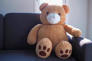 teddybären sitzen auf dem sofa im haus mit einer in covid-19 geschriebenen maske. die situation der virus covid19-infektion breitet sich auf der ganzen welt aus. foto