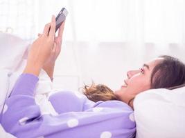 frau, die im bett im schlafzimmer liegt, entspannt online-spiele spielt und serien korea online mit einem smartphone anschaut, während sie introvertiert ist, zu hause bleibt und nicht nach draußen geht. foto