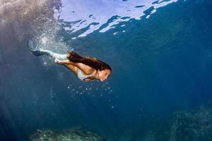 Meerjungfrau, die unter Wasser im tiefblauen Meer schwimmt foto