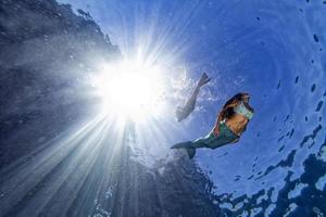 Meerjungfrau, die unter Wasser im tiefblauen Meer schwimmt foto