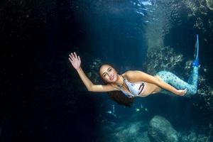 meerjungfrau, die mit tauchern im tiefblauen meer unter wasser schwimmt foto