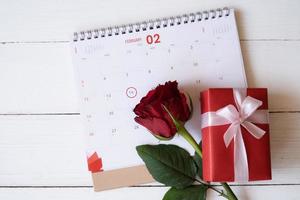 rote Rose und rote Geschenkbox auf dem Kalender lokalisiert auf weißem hölzernem Hintergrund mit. Valentinstag-Konzept. planung terminplaner, veranstaltung, organisator valentinstag. flache Lage, Draufsicht. foto