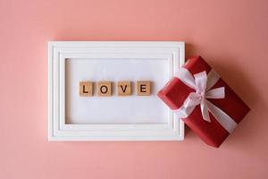 rote geschenkbox und fotorahmen mit buchstabenworten der liebe auf rosa hintergrund zum verschenken im urlaub mit kopienraum für text. Feiertage, Geschenke, Schenken. neujahrstag, weihnachtstag, chinesisches neujahr. foto