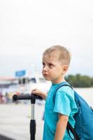 ein Junge auf einem Roller am Ufer der Stadt entlang. Reise. Rucksack auf dem Rücken. Das Gesicht drückt natürliche freudige Emotionen aus. nicht inszenierte Fotos aus dem Leben