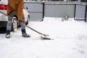 ein mann im winter reinigt schnee mit einer schaufel im hof eines hauses auf dem parkplatz. Schneefall, schwierige Wetterbedingungen, das Auto stockt, gräbt die Passage auf foto