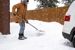 ein mann im winter reinigt schnee mit einer schaufel im hof eines hauses auf dem parkplatz. Schneefall, schwierige Wetterbedingungen, das Auto stockt, gräbt die Passage auf foto