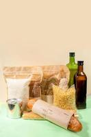 Vorrat an Lebensmitteln in Papier- und Zellophanverpackungen auf beige-grün. Müsli, Nudeln, Ölflaschen, Blechdose, Brot. foto