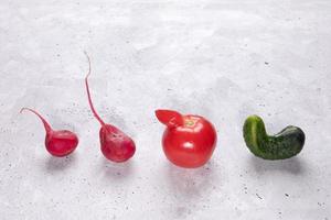vier hässliche gemüse tomaten, gurken und rettich, die in reihe auf betonhintergrund ausgelegt sind. foto