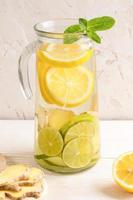Glaskaraffe mit Wasser, angereichert mit Zitrone, Limette und Ingwer auf hellem Hintergrund. foto