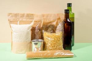 Vorrat an Lebensmitteln in Papier- und Zellophanverpackungen auf beige-grünem Hintergrund. Müsli, Nudeln, Ölflaschen. Nahaufnahme. foto