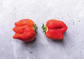 Zwei hässliche Erdbeeren liegen auf grauem Betongrund. foto