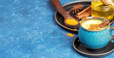 Blaue Tasse indisches ayurvedisches gesundes Getränk - goldene Kurkuma-Latte-Milch und Teller mit Zutaten auf Blau. Platz kopieren. foto
