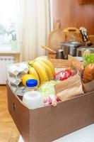 Karton mit Lebensmitteln auf Küchentisch im Innenraum. sichere Lieferung. Lebensmittelspende. Weicher Fokus. foto