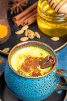 Nahaufnahme blaue Tasse traditioneller indischer ayurvedischer goldener Kurkuma-Milch mit Zutaten auf Teller auf blauem Hintergrund. foto