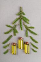 Grüne Fichtenzweige und kleine Glasflaschen mit ätherischem Tannenöl, die als Weihnachtsbaum auf grau strukturiertem Hintergrund ausgelegt sind. foto