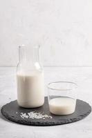 Trinkglas und Glasflasche mit gesunder Reismilch auf rundem Schieferbrett auf weißem Hintergrund. foto