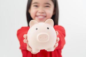 kleines asiatisches mädchen, das geld in einem sparschwein spart, über sparen lernt, kind spart geld für zukünftige bildung. geld, finanzen, versicherungen und personenkonzept foto