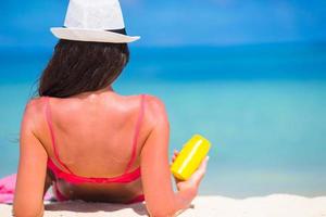 Frau, die Sonnenschutzflasche an einem Strand hält foto