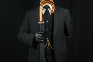 Porträt eines Mannes in dunklem Anzug und Lederhandschuhen, der einen Regenschirm wie ein Gewehr auf schwarzem Hintergrund hält. klassischer britischer Gentleman foto