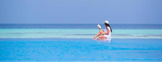 Frau, die ein Buch liest, während sie am Rand eines Schwimmbades sitzt foto