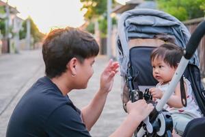 asiatischer vater und tochter oder sohn süßes mädchen, das spiel macht, sich glücklich fühlt und auf kinderwagen genießt vater und sohn blickkontakt lächeln, so dass familienliebe abend mit sonnenlicht auf gesichtsglück zeigt foto