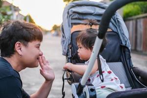 asiatischer vater und tochter oder sohn süßes mädchen, das ein high five macht und sich glücklich fühlt und auf dem kinderwagen genießt vater und sohn blickkontakt lächeln und so familienliebe abend mit sonnenlicht im gesicht glück zeigen foto