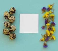 Osterkomposition. Wachteleier, Blumen, weißes Papier leer auf blauem Hintergrund. Platz kopieren. foto