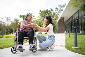 asiatische vorsichtige pflegekraft oder krankenschwester halten die hand des patienten und ermutigen den patienten im rollstuhl. Konzept des glücklichen Ruhestands mit Betreuung durch eine Pflegekraft und Spar- und Seniorenkrankenversicherung. foto