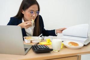 Beschäftigte und müde Geschäftsfrau, die Spaghetti zum Mittagessen im Büro isst und daran arbeitet, einem Chef Jahresabschlüsse zu liefern. überarbeitet und ungesund für Fertiggerichte, Burnout-Konzept. foto