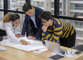 Das multiethnische Diversity-Business-Designer-Team arbeitet gemeinsam an der Blaupause in modernen Büroräumen mit Laptop-Computer und Papierkram auf dem Schreibtisch. foto