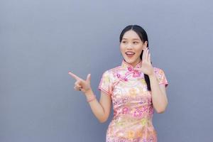 schöne asiatische frau mit langen haaren, die rosa cheongsam-kleid im chinesischen neujahrsthema trägt, während ihre hand zeigt, um etwas zu präsentieren und hand zu zeigen foto